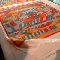 In preparation for printing, the silk for the scarves is rolled out and affixed to a waxed board.