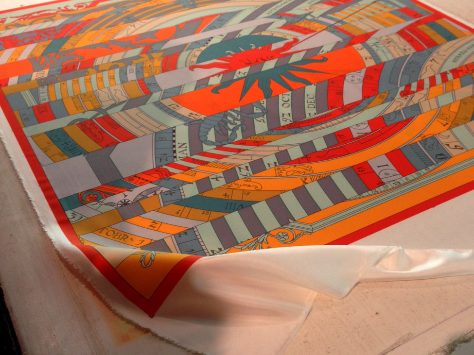 In preparation for printing, the silk for the scarves is rolled out and affixed to a waxed board.